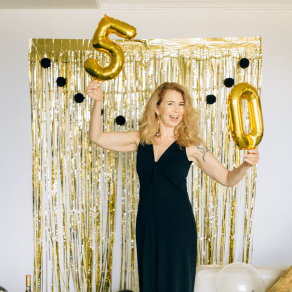 Donna over 50 con trucco professionale tiene palloncini a forma di 5 e 0 per il suo 50esimo compleanno.