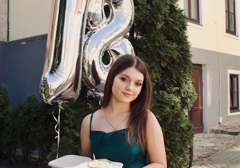 Ragazza al suo diciottesimo compleanno con trucco di Noemi Spera Make Up Artist, tiene una torta con due palloncini a forma di "18" sullo sfondo.